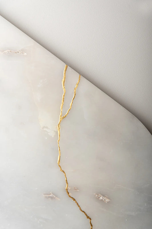 Broken pieces of white marble reassembled with gold, inspired by the Kintsugi technique, which emphasizes the beauty and strength found in imperfections.