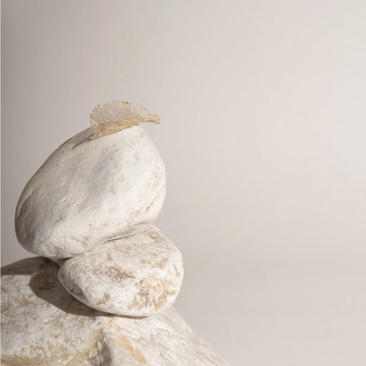 Three smooth, white stones stacked vertically, with a delicate, translucent leaf resting on the top stone, symbolizing the fine lines and delicate texture of skin.