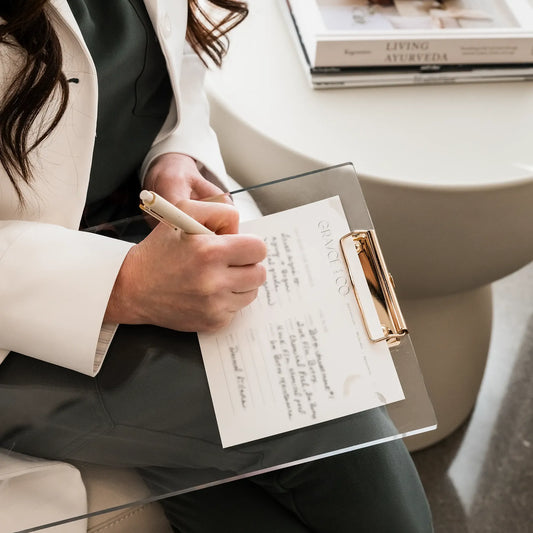 A cosmetic dermatology specialist in a white coat at Grayce Skin Co. in Knoxville, TN sits on a chair, jotting notes in her notepad, focused and professional.